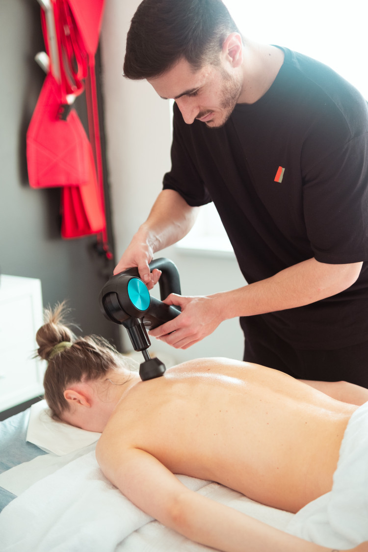 Ein Therapeut führt mit einem Massagegerät eine Behandlung an der Rückenpartie einer liegenden Person durch.